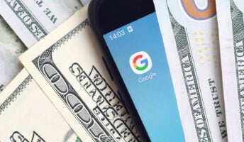 Phone with Google icon nestled in middle of US dollar bills illustrating Google and money