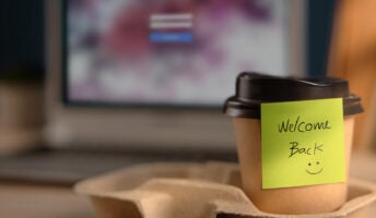 Coffee cup with note saying "Welcome Back" on desk illustrating return to office concept