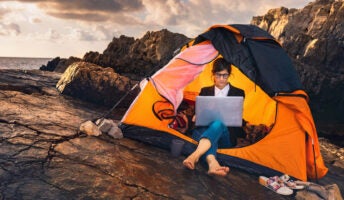 Woman sitting working remotely on laptop in tent on mountain