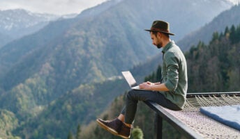 Young man in hat working remotely whilst travelling in beautiful mountain area