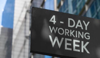 Sign displaying the words 4-day working week against a backdrop of downtown city buildings.