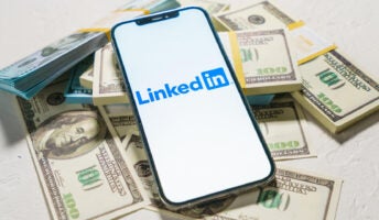 LinkedIn logo open on smartphone resting on pile of money