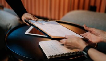 HR representative exchanges paperwork with someone over table illustrating HR software pricing