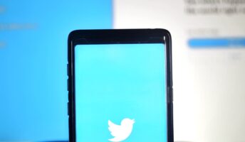 The Twitter logo on a smartphone, being held in front of a screen